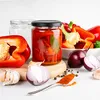 A collection of ingredients and a jar of preserved food, likely peppers, are arranged on a white surface with a light gray background. Produktbild-Vorschau