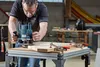 A man is using a router on a piece of wood on a workbench in a workshop. Náhľad obrázku produktu