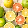 A top-down view of various citrus fruits, some whole and some sliced, arranged on a wooden surface. Podgląd zdjęcia produktu