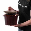 A person is holding a brown ceramic pot with a lid. Voir les images du produit