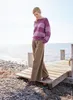 A woman stands on a wooden pier by the sea, wearing a striped sweater and wide-leg pants. Produktbild-Vorschau