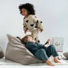 Two children are interacting in a room with a beanbag chair. One child is sitting on the beanbag reading a book, while the other child is standing and jumping. Anteprima dell’immagine prodotto