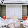 A wooden snow shovel leans against a garage door in a snowy environment. Náhled obrázku produktu