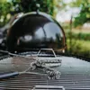 A close-up of a grill grate with a grill brush on it, with the lid of a black grill in the background. Produktbild-Vorschau