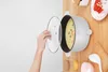 A hand is lifting the lid of a white electric pot filled with soup, placed on a wooden table with other kitchen items. Produktbild-Vorschau