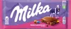 A Milka chocolate bar with colorful candy-coated chocolate pieces inside, set against a purple and pink background with mountains and a cow illustration. Produktbild-Vorschau