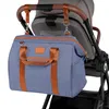 A blue diaper bag with brown accents is attached to the handle of a stroller. Náhľad obrázku produktu
