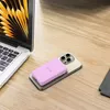 A pink power bank is placed on top of a gold smartphone, next to a laptop on a wooden desk. Náhled obrázku produktu