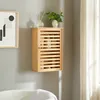 A wooden bathroom cabinet with a slatted door is mounted on a gray wall above a white bathtub. Decorative items, including a plant and diffuser, are placed on top of the cabinet. Anteprima dell’immagine prodotto