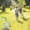 A father and son are playing in the garden with a hose, spraying water on each other. The image also shows a close-up of a water pump with stones and water splashing. Produktbild-Vorschau