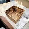 A wooden crate sits on a light-colored surface, with a piece of white fabric to the right and a wooden beam to the left. Anteprima dell’immagine prodotto