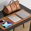 A brown duffel bag and various electronic devices are arranged on a black marble desk with a brown desk mat. Anteprima dell’immagine prodotto
