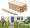 A stack of wooden stakes with one stake in the foreground, and a garden scene with a house in the background. Náhled obrázku produktu