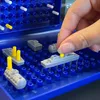A hand is placing a yellow peg into a miniature ship on a blue game board, which is part of a Battleship game. Náhľad obrázku produktu