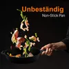 A hand holding a black frying pan with food ingredients flying out of it, against a black background. Produktbild-Vorschau