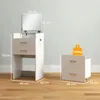 A white vanity table with a mirror and a matching nightstand are shown in a room with a light gray wall and a wooden floor. Produktbild-Vorschau