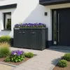 A modern house exterior with a dark gray trash bin enclosure featuring a planter box filled with purple flowers. The enclosure is placed on a paved walkway next to the house entrance. Náhľad obrázku produktu