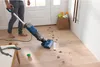 A person is using a wet and dry vacuum cleaner to clean muddy paw prints on a wooden floor near a doorway. A dog leash and ball are on the floor nearby. Podgląd zdjęcia produktu
