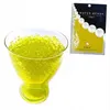 A glass bowl filled with yellow-green water beads next to a package of water beads. Produktbild-Vorschau