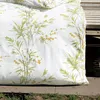 A close-up of a white duvet cover with a green bamboo and yellow flower pattern, placed on a wooden deck next to a concrete border and grass. Produktbild-Vorschau