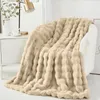 A plush blanket draped over a white armchair, with a small cabinet and a lamp in the background. Produktbild-Vorschau