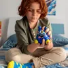 A child is sitting on a bed, holding a blue monster toy. Voir les images du produit