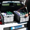 The back of a car with two folding crates filled with water bottles and other items. Produktbild-Vorschau