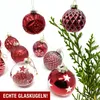 A collection of red glass Christmas ornaments arranged with a sprig of evergreen on a white background. Produktbild-Vorschau