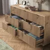 A wooden sideboard with several drawers open, revealing folded clothes inside, in a room with wooden flooring and curtains. Voir les images du produit