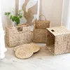 Several woven storage baskets and round placemats are arranged on a light-colored wooden floor, with a framed abstract artwork and a vase of greenery in the background. Anteprima dell’immagine prodotto