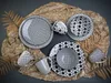 A collection of black and white patterned ceramic plates and mugs arranged on a textured brown surface, with dried leaves on the sides. Produktbild-Vorschau