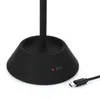 Close-up of the base of a black LED table lamp, showing a USB-C port and a red charging indicator light, with a USB-C cable plugged in. Produktbild-Vorschau