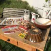 A collection of baking supplies and finished cookies are arranged on a wooden table outdoors. Produktbild-Vorschau