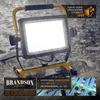 A work light is shown in a rainy outdoor environment, with text overlays highlighting its features and specifications. Produktbild-Vorschau