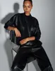 A woman is sitting on a chair, wearing a black leather jacket and pants. Produktbild-Vorschau