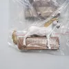 A white horse figurine is lying on a brown rectangular base, inside a clear plastic bag. Náhľad obrázku produktu