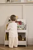 A young child is looking at books on a white bookshelf. Produktbild-Vorschau