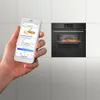A hand holding a smartphone with an oven app open, next to a built-in oven with food inside. Anteprima dell’immagine prodotto