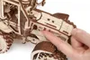A close-up shot of a wooden 3D puzzle of a tractor, with a person's finger touching a part of the model. Náhľad obrázku produktu