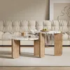 A set of two round terrazzo coffee tables with wooden legs are placed on a light-colored rug in front of a tufted cream sofa. Voir les images du produit