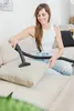 A woman is vacuuming a cushion on a sofa. Produktbild-Vorschau