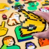 A hand holding a yellow and black perler bead creation, with other perler bead creations in the background. Produktbild-Vorschau