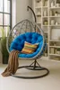A hanging egg chair with a blue cushion and a brown blanket is placed in a room with a bookshelf in the background. Anteprima dell’immagine prodotto