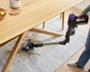 A person is vacuuming a rug under a wooden table with a cordless vacuum cleaner. Anteprima dell’immagine prodotto
