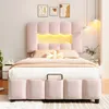 A pink upholstered bed with a scalloped headboard featuring integrated LED lighting, set in a bedroom with decorative artwork and pendant lights. Produktbild-Vorschau