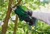 A person's hand wearing a glove is holding a green electric pruning shear and cutting a tree branch. Produktbild-Vorschau