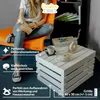 A person is sitting on an orange chair next to a white wooden crate table. The table has a book, a vase, and a candle on it. The scene is indoors. Produktbild-Vorschau