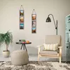 A living room scene featuring a chair, a plant, a side table with books and a mug, and two hanging photo frames. Produktbild-Vorschau