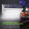 A solar-powered outdoor light is mounted on a wall, with rain falling. The background shows a blurred image of a modern house at night. Produktbild-Vorschau