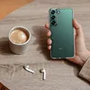 A hand holding a green smartphone case next to a cup of coffee and wireless earbuds on a wooden table. Anteprima dell’immagine prodotto